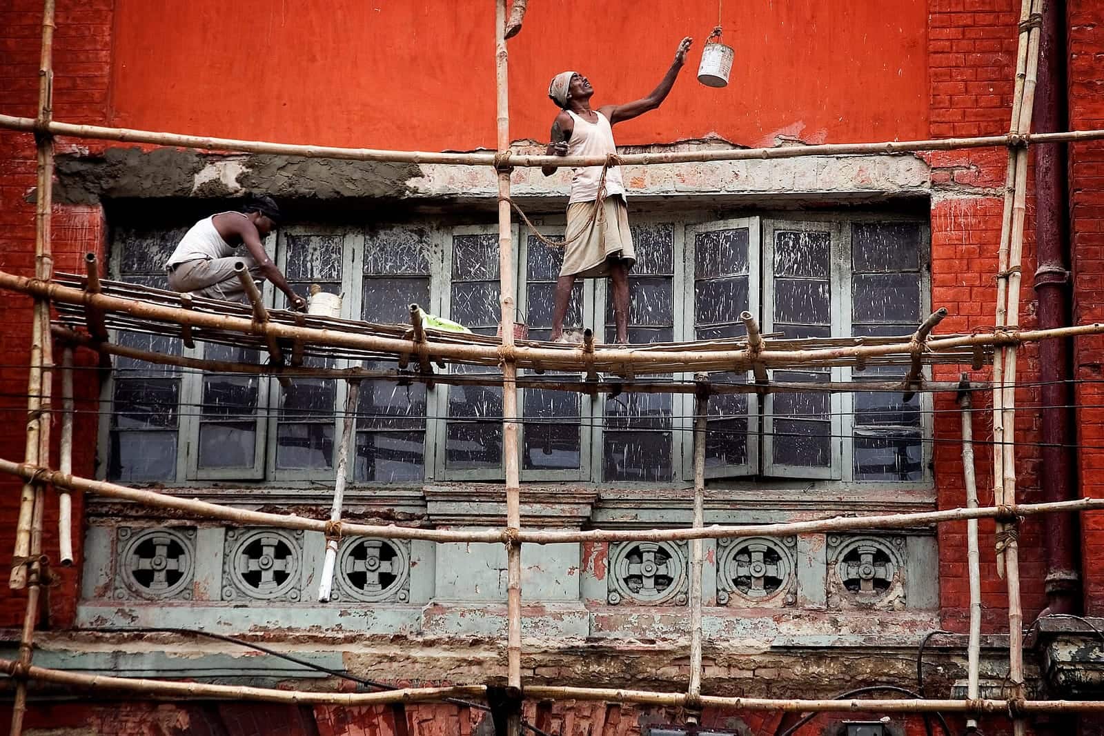 Workers on bamboo scaffolding against a painted brick façade