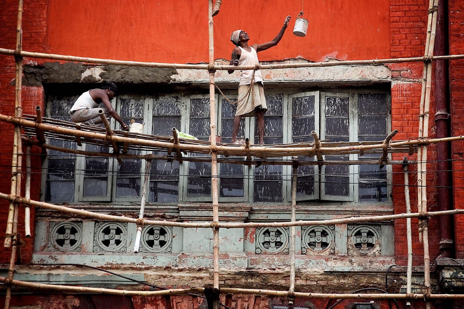 Workers on bamboo scaffolding against a painted brick façade